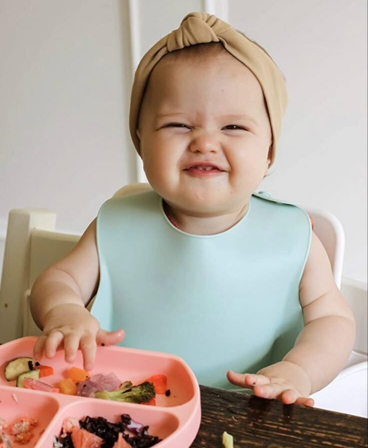 Seated in a cozy high chair, the baby eagerly grabs a handful of food, tiny fingers exploring each bite. With a messy yet joyful face, they giggle between bites, savoring the new flavors. A moment of discovery, growth, and pure delight!