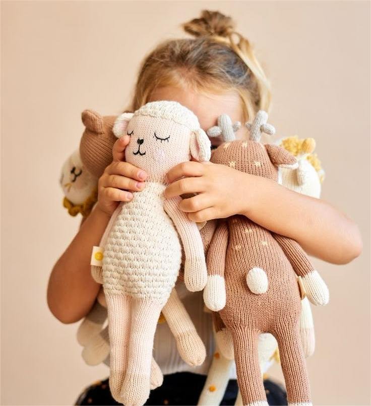 A happy baby hugging a bunch of soft toys with tiny arms, eyes sparkling with joy and comfort.