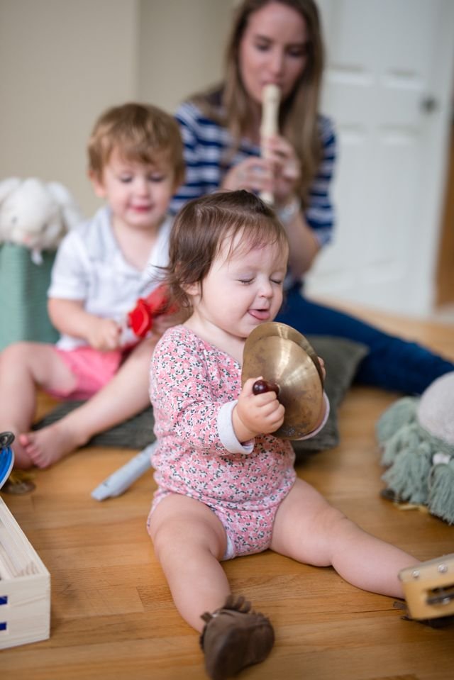  two babies are joyfully playing with a colorful music toy, their curious eyes lit up with excitement. Their mother smiles lovingly as she guides them, sharing a moment of fun and learning through music. It’s a heartwarming scene of play, bonding, and discovery.