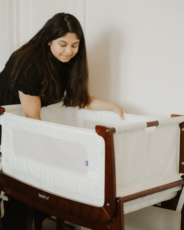 A loving mother gazes adoringly at her baby, nestled peacefully in a cozy bassinet.